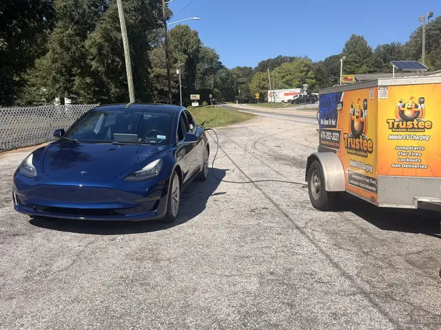 Blue Tesla sedan beside the Trustee branded mobile EV charging trailer outdoors in daylight