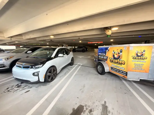 White BMW i3 parked beside the Trustee branded mobile EV charging trailer inside a parking garage