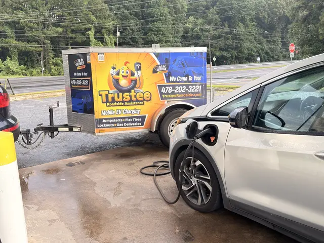Silver electric hatchback plugged in to Trustee mobile charging equipment next to the Trustee trailer