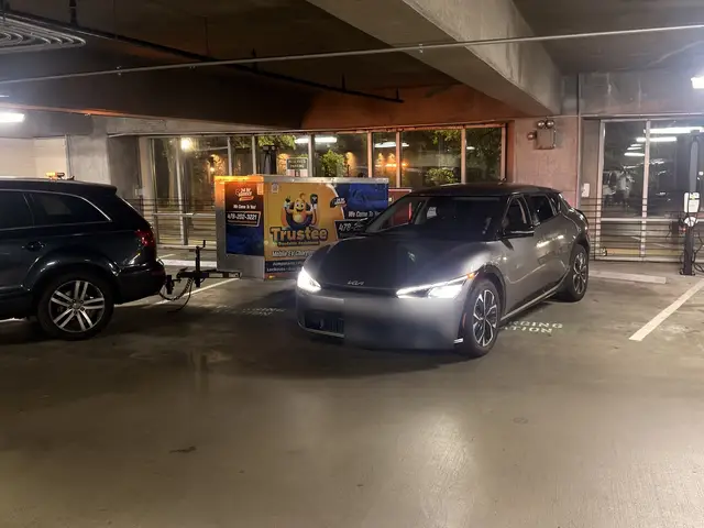 Silver Kia electric vehicle parked beside the Trustee charging trailer in a parking garage