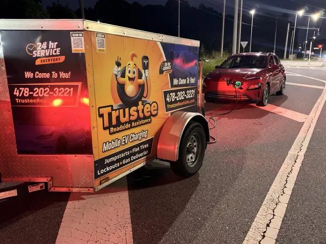 Red electric crossover plugged in to the Trustee mobile EV charging trailer at night beside a road